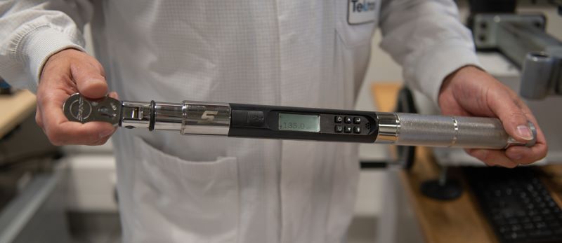Torque wrench calibration A calibration technician in a white lab coat holds a digital torque wrench horizontally, with the display screen showing