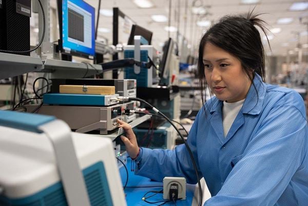Female service technician working on test and measurement equipment in an engineering lab.