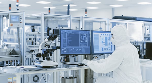 Semiconductor scientist in protective clothes doing research on a personal computer while in a semiconductor fabrication facility.